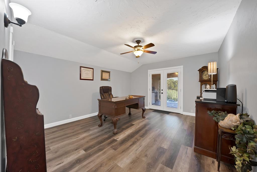 Vaulted ceilings, wood-finish flooring, central ceiling fan with integrated lighting, wall-mounted sconce, and glass-paneled double doors