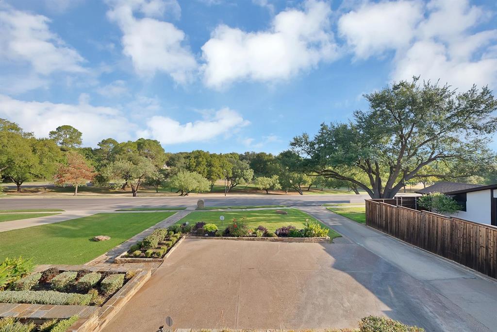 Concrete driveway, tiered stone-bordered landscaping, manicured lawn, and wood-finish perimeter fencing
