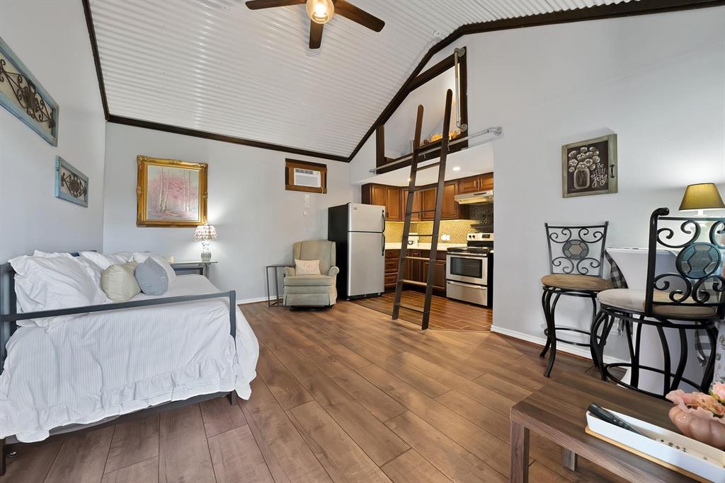 Vaulted ceiling with corrugated metal finish, wood-finish flooring, loft area with access ladder, and kitchen with dark-finish cabinetry