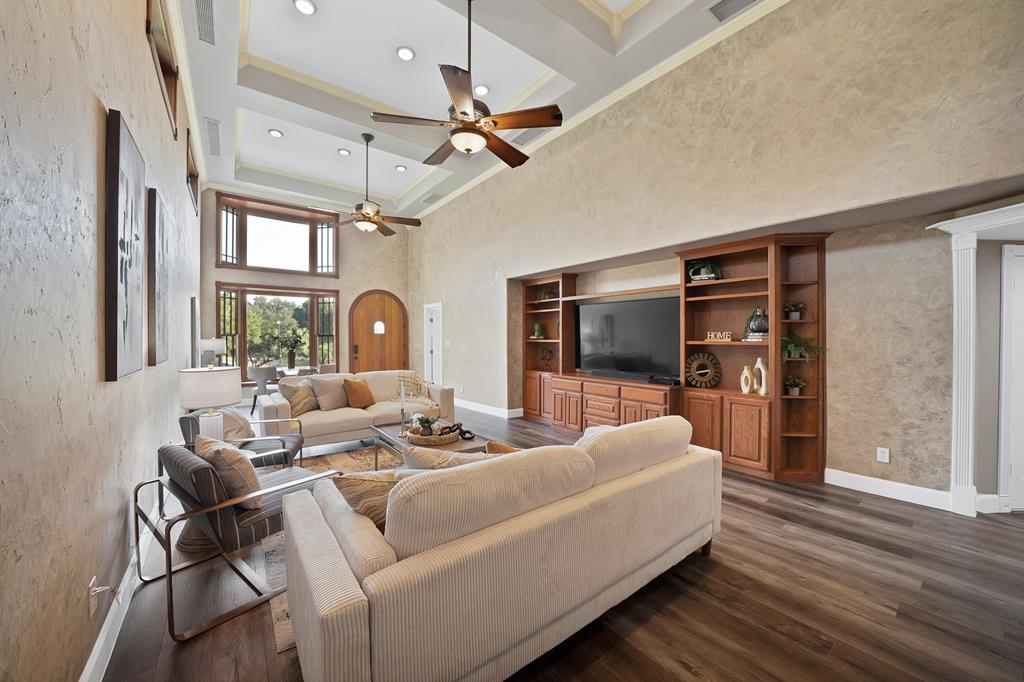Living area featuring double-height ceilings with a coffered design, built-in wooden cabinetry with integrated shelving, wood-finish flooring, and multi-pane windows
