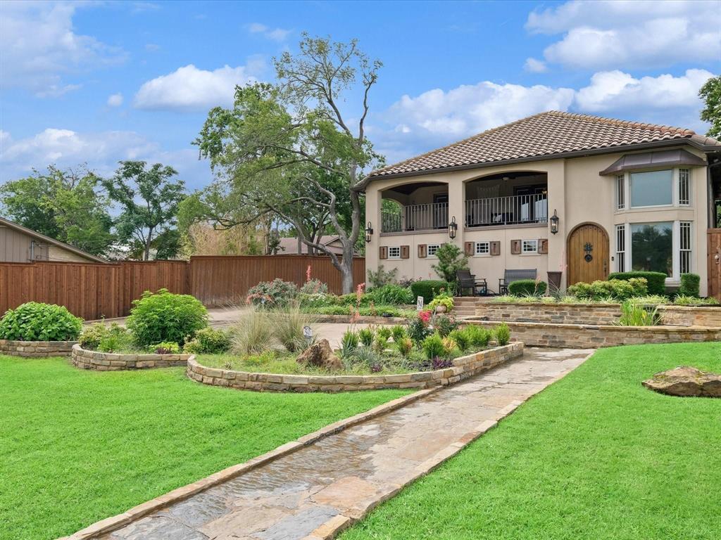 Two-story residence featuring a tile roof, stucco exterior, covered balcony, arched wooden front entry door, and tiered stone landscape retaining walls