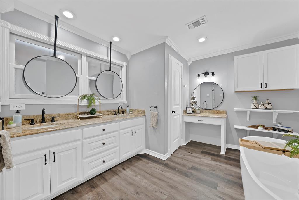 Dual-vanity cabinetry with stone countertops, suspended circular mirrors, wood-finish flooring, built-in vanity station, and wall-mounted shelving