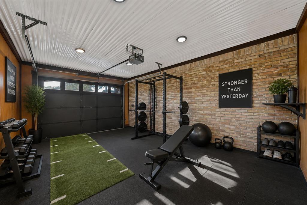 Multi-use space featuring corrugated metal ceiling panels, exposed brick wall, rubberized flooring, recessed lighting, and a multi-panel garage door