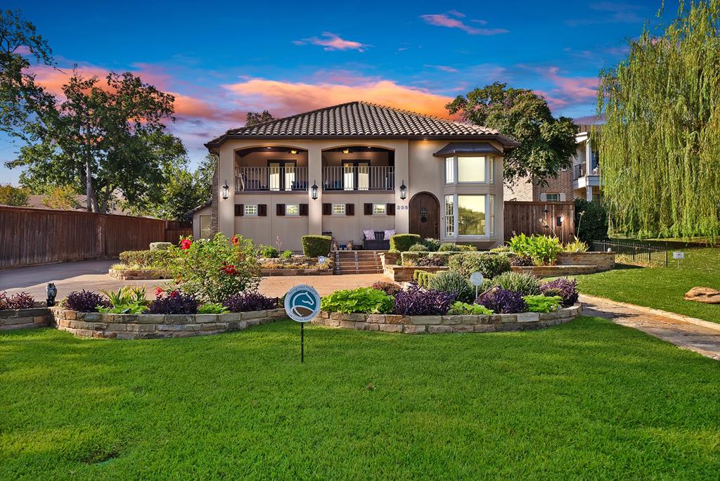 Two-story residence featuring a tile roof, an upper-level covered balcony, a bay window, and tiered stone landscaping with integrated garden beds