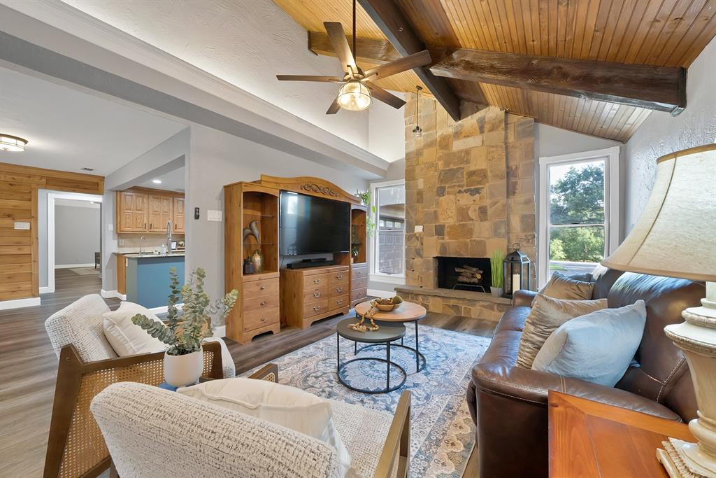Vaulted ceiling featuring wood-plank paneling and exposed structural beams, floor-to-ceiling stone fireplace, and wood-finish flooring