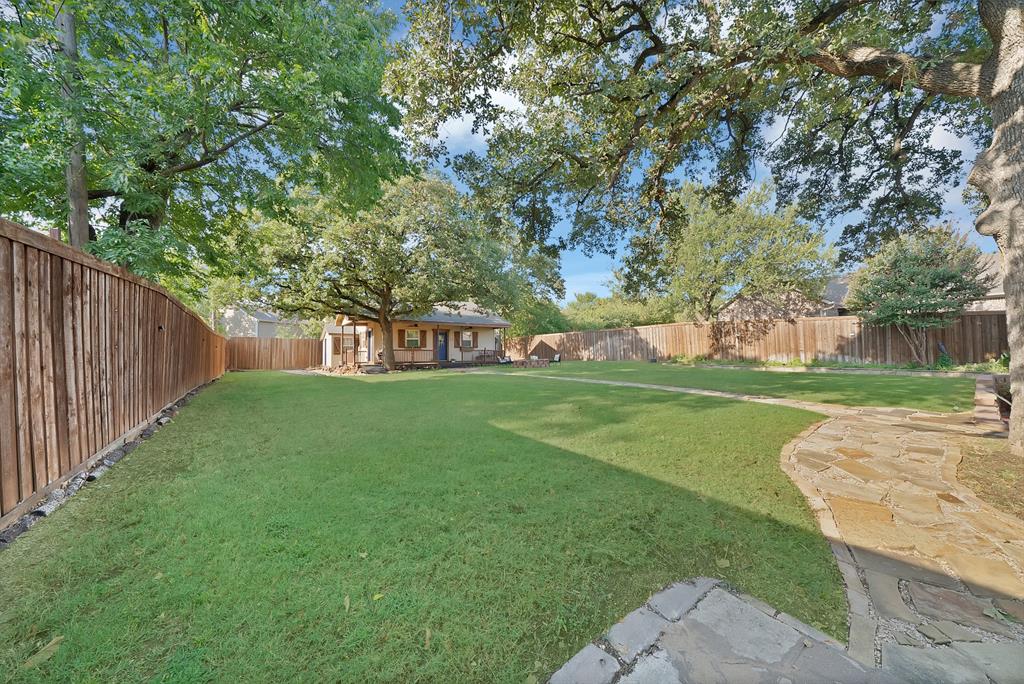 Expansive backyard featuring a large grass lawn, perimeter wood fencing, flagstone path, and mature shade trees
