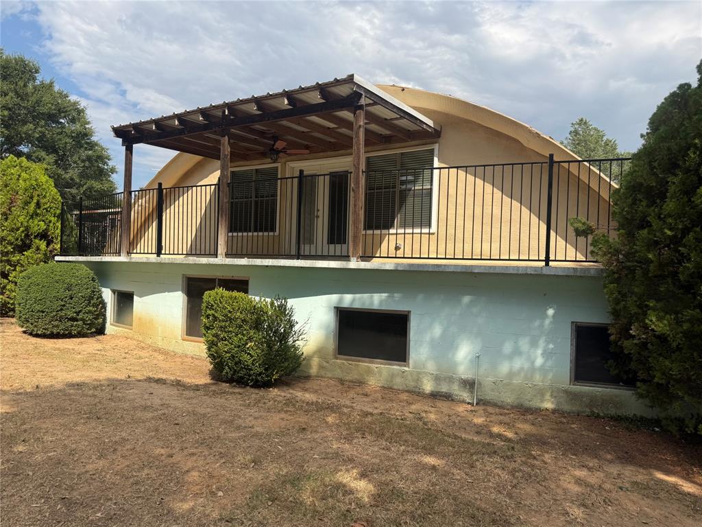 Quonset architectural roofline featuring an elevated deck with metal railing, a covered patio structure with a ceiling fan, and ground-level windows