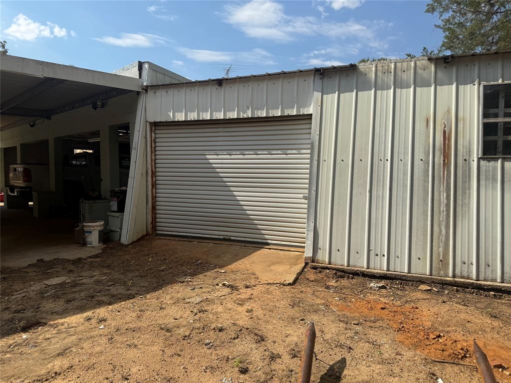 Metal-sided outbuilding featuring a roll-up garage door and an attached open-air carport