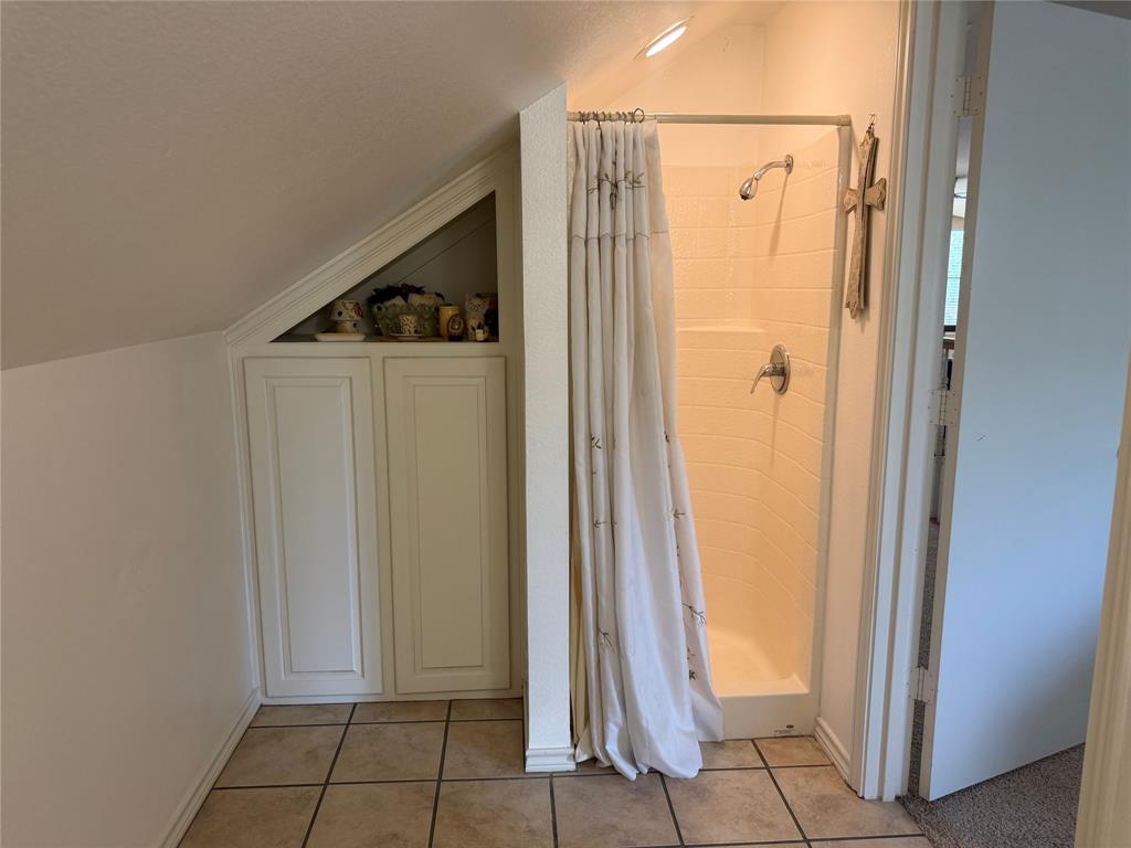 Shower stall featuring molded surround and metal fixtures, accompanied by built-in under-eave cabinetry with recessed shelving and tile flooring