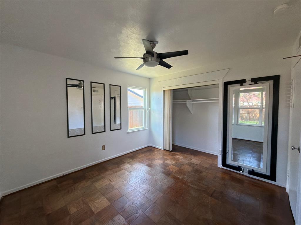 Parquet wood-finish flooring, ceiling fan with integrated lighting, built-in closet with sliding door, and wall-mounted rectangular mirrors