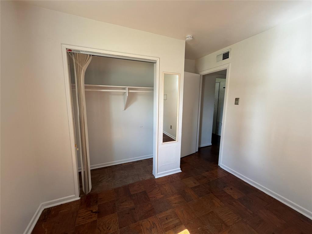 Parquet wood-finish flooring throughout, closet featuring a built-in shelf and hanging rod, and a recessed wall-mounted mirror
