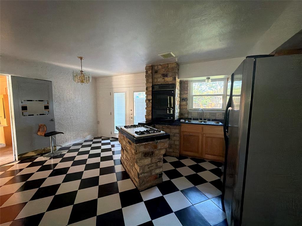 Kitchen featuring a prominent stone-clad central island with an integrated cooktop, double wall ovens, wood cabinetry, and a checkered tile floor