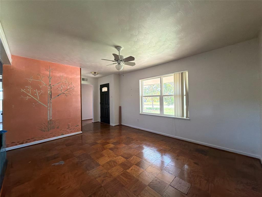Parquet wood-finish flooring, accent wall with decorative mural, ceiling fan with integrated light fixture, and multipane window