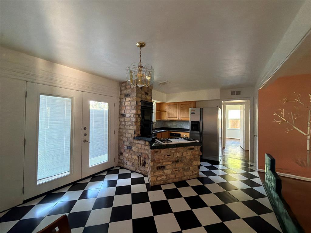 Checkerboard tile flooring, brick-surround cooking island, dual glass-paneled exterior doors, and a multi-arm metal chandelier