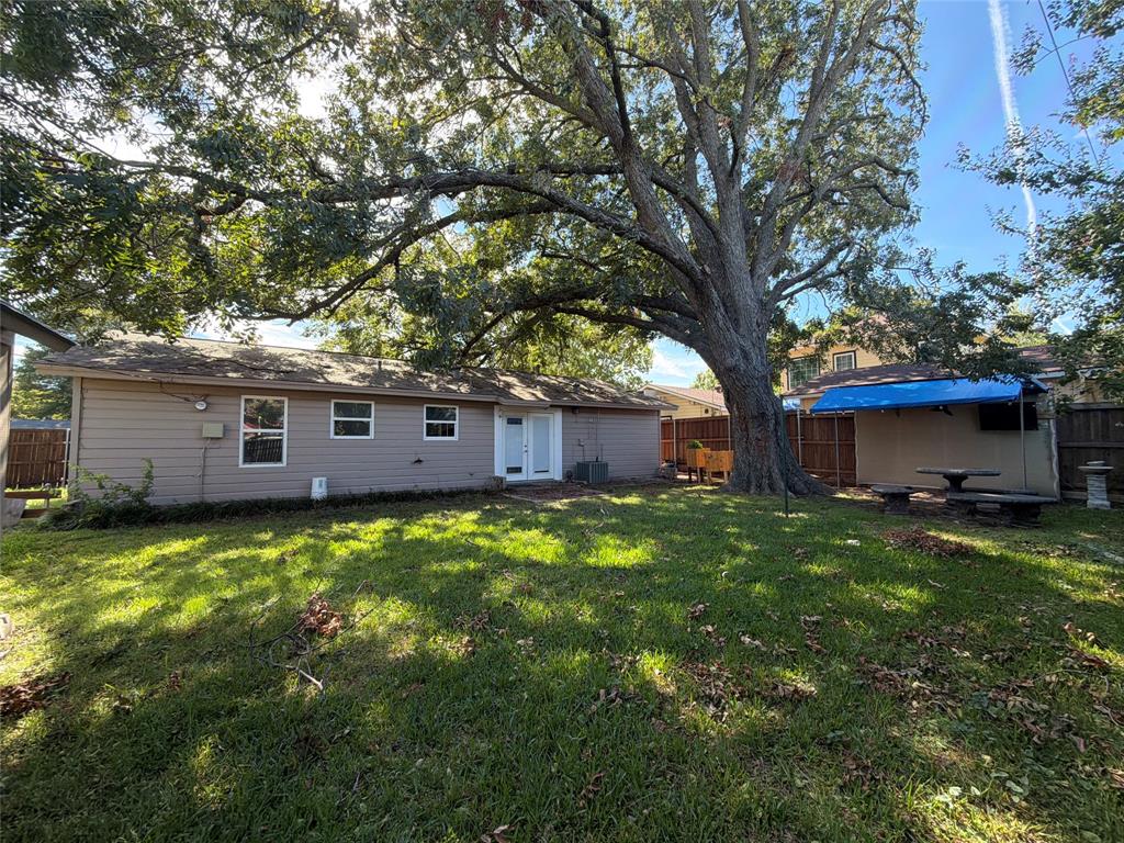 Expansive backyard featuring a mature canopy tree, wood-paneled exterior siding, a covered patio structure, and perimeter privacy fencing