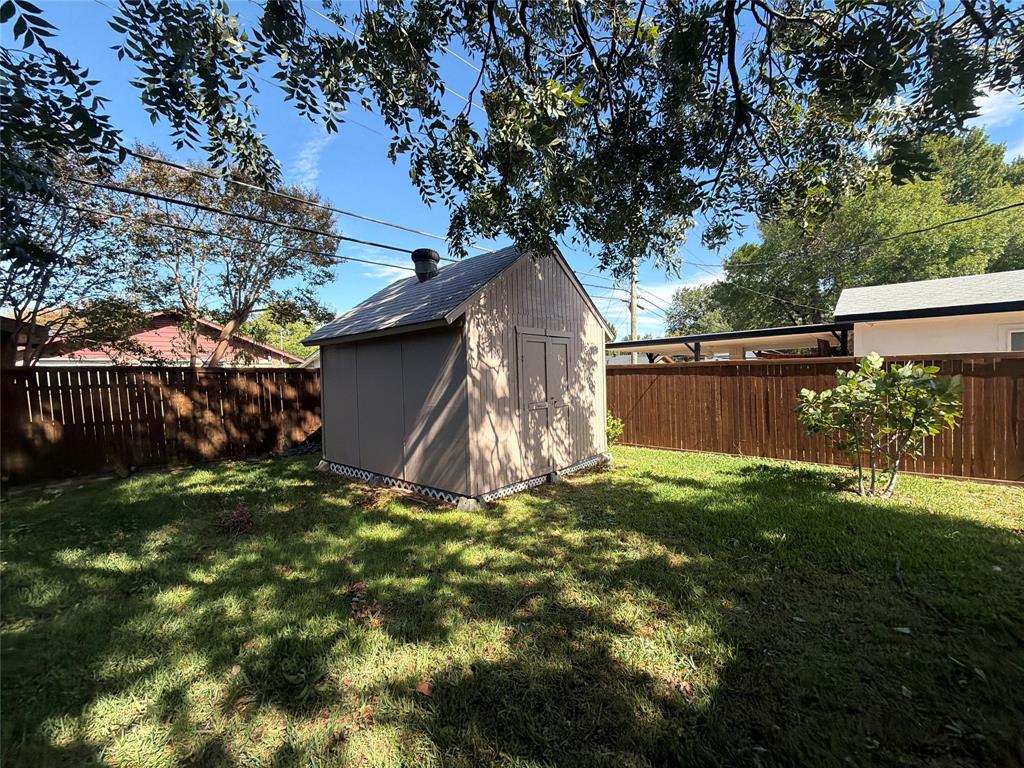 Detached storage structure featuring vertical siding, a pitched roof, and double-door entry, situated within a fenced backyard