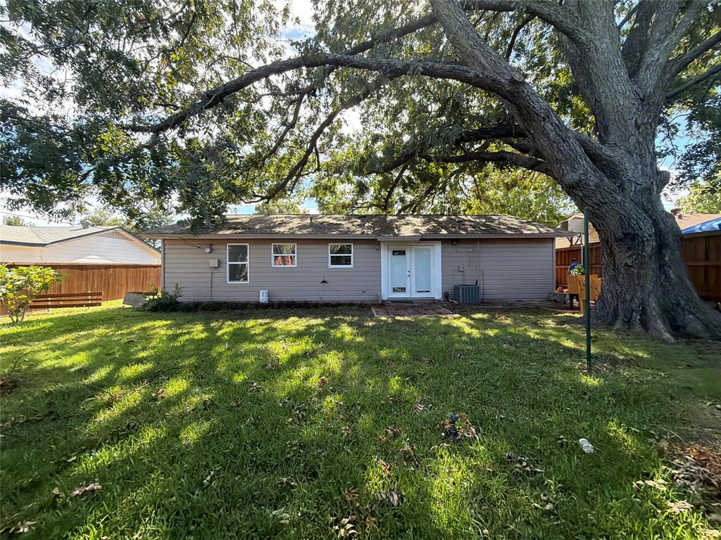Rear exterior featuring horizontal siding, double glass-paneled entry doors, a mature tree, and wood privacy fencing