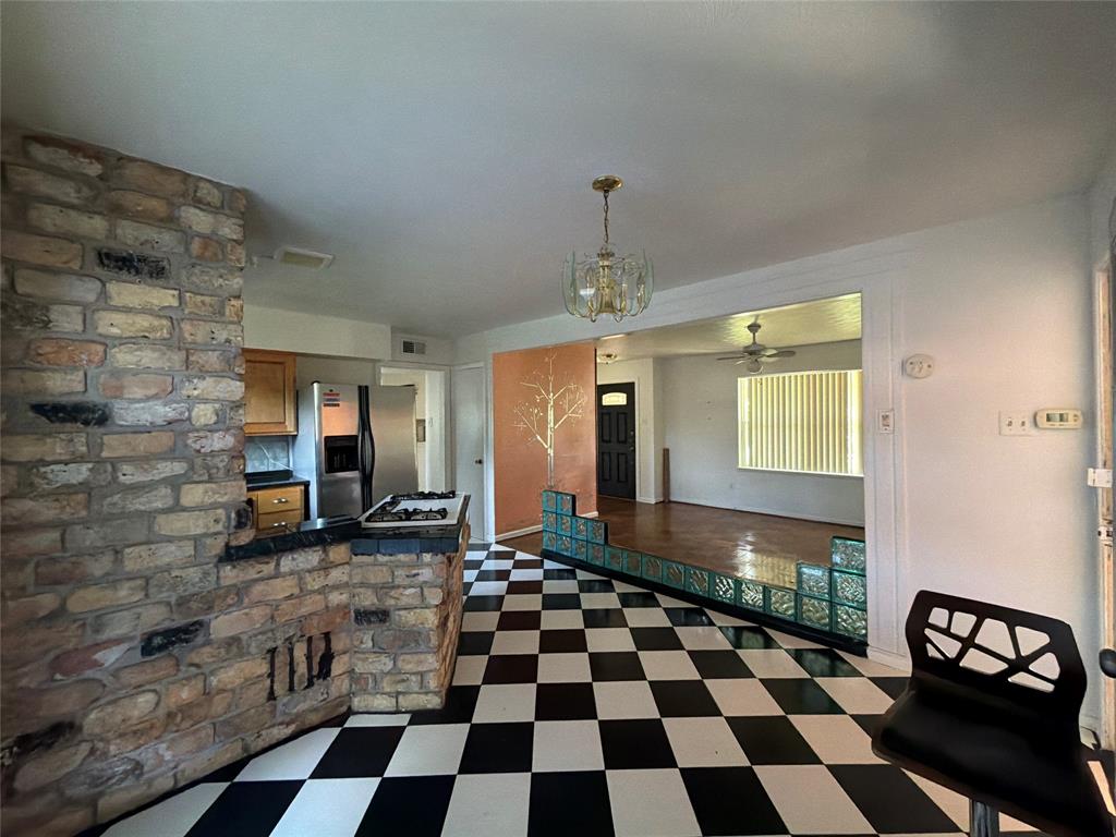 Interior space featuring a floor-to-ceiling multi-tonal brick fireplace, black-and-white checkered flooring, decorative glass block partitions, wood-finish flooring, and a multi-arm brass chandelier