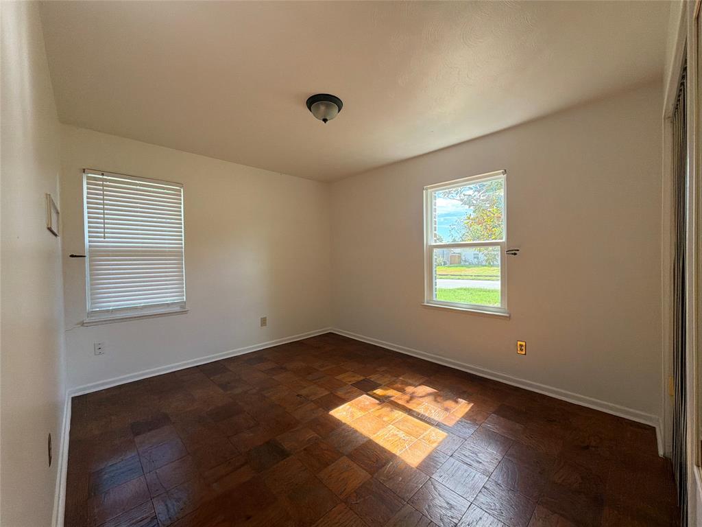 Room featuring parquet wood-finish flooring, two windows with blinds, and a flush-mount ceiling light fixture