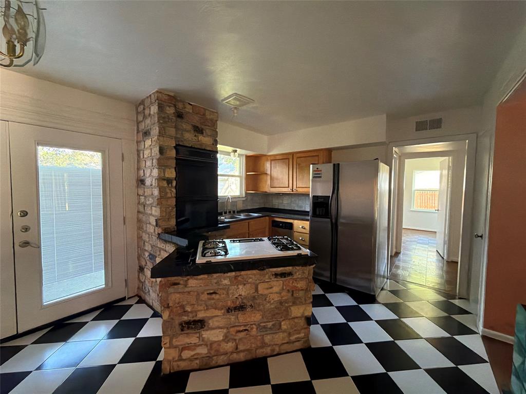 Kitchen featuring a brick-encased built-in cooktop and oven, wood cabinetry, stone-finish countertops, stainless steel side-by-side refrigerator, and checkerboard tile flooring