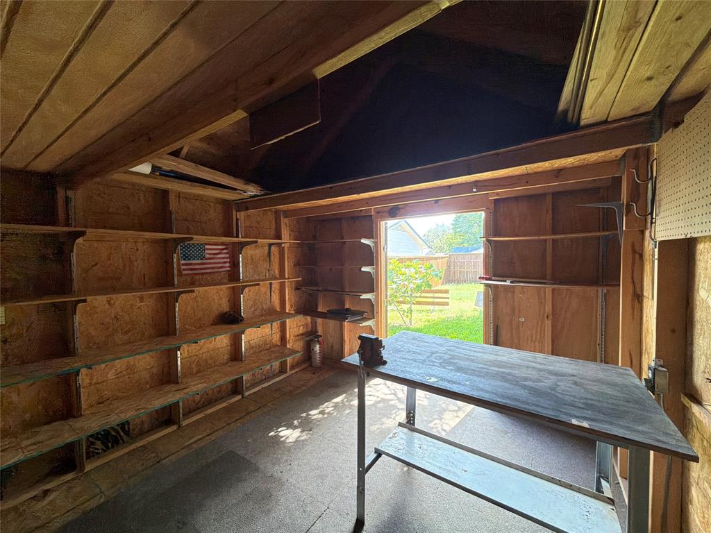 Outbuilding featuring wood-paneled walls, multiple rows of built-in shelving, vaulted ceiling, and a stationary workbench