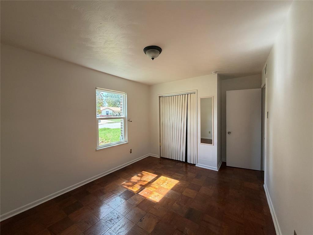 Interior room featuring parquet wood-finish flooring, a double-door closet with vertical sliding panels, a wall-mounted mirror, a single-pane window, and a central ceiling-mounted light fixture