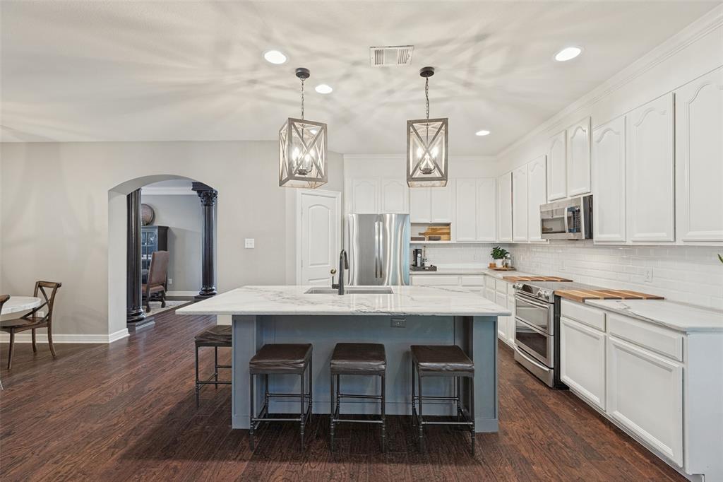 Kitchen featuring white cabinetry, stone-surface central island with integrated sink, stainless steel appliances, wood-finish flooring, and pendant lighting