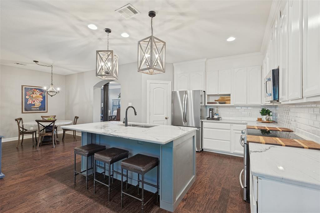 Kitchen featuring white cabinetry, a center island with a Quartzite countertop, stainless steel appliances, geometric pendant lighting, and wood-finish flooring