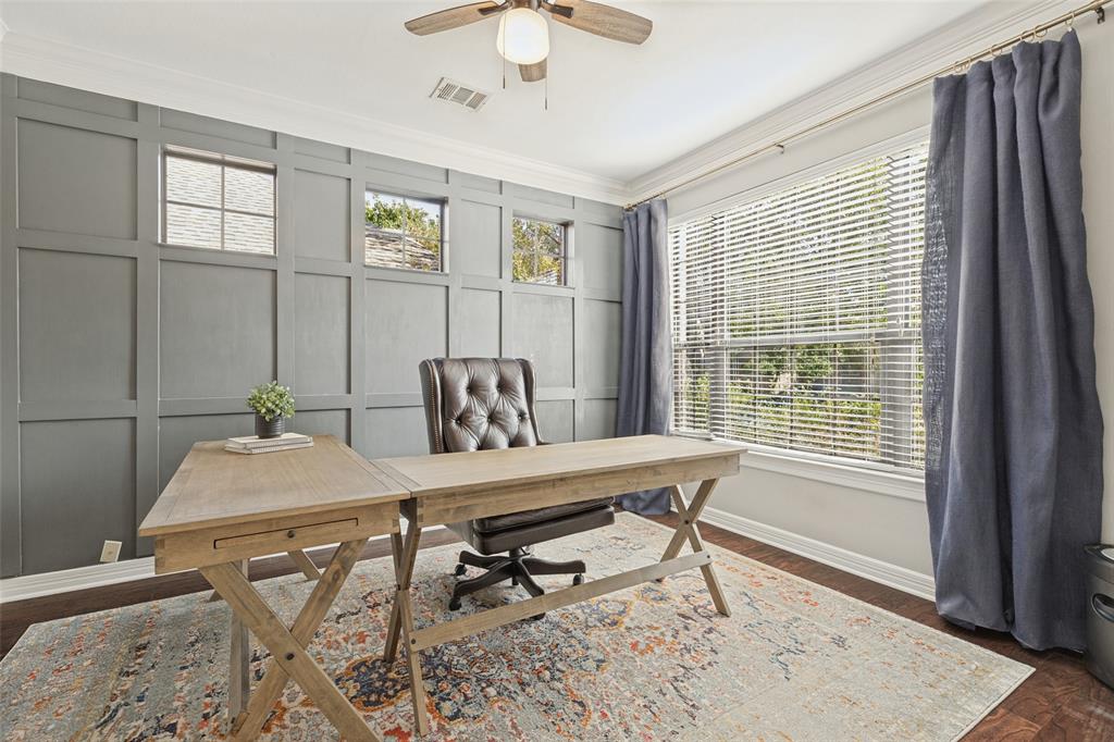 Accent wall with grid-pattern millwork, large window with horizontal blinds, crown molding, and ceiling fan with integrated lighting