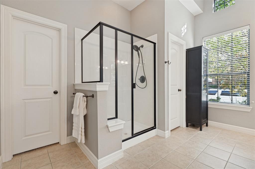 Walk-in shower featuring a glass enclosure with matte black framing, a handheld showerhead, a built-in bench, and ceramic tile flooring