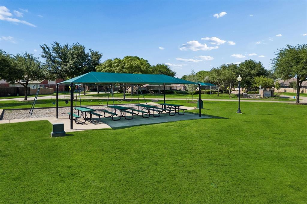 Outdoor green space featuring a covered pavilion, concrete patio, metal picnic tables, and walking paths