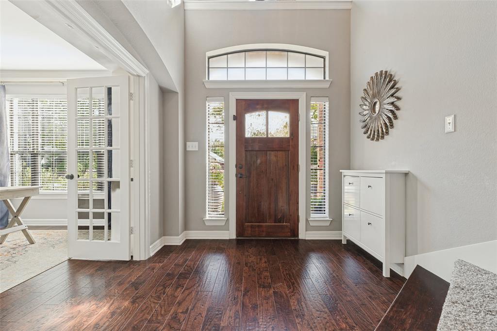 Entryway featuring dark-stained wood-finish flooring, a solid wood front door with a glass inlay, a transom window, and white-painted French doors