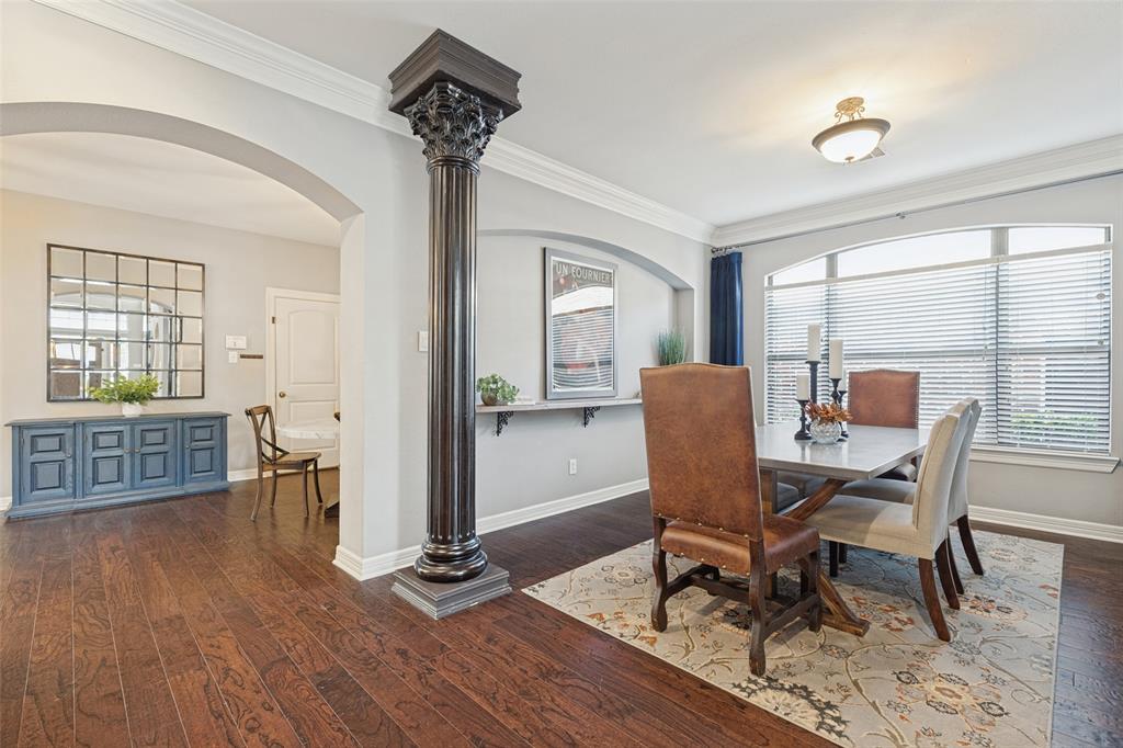 Decorative column featuring ornate detailing, wood-finish flooring, crown molding, arched architectural opening, and a built-in recessed wall niche