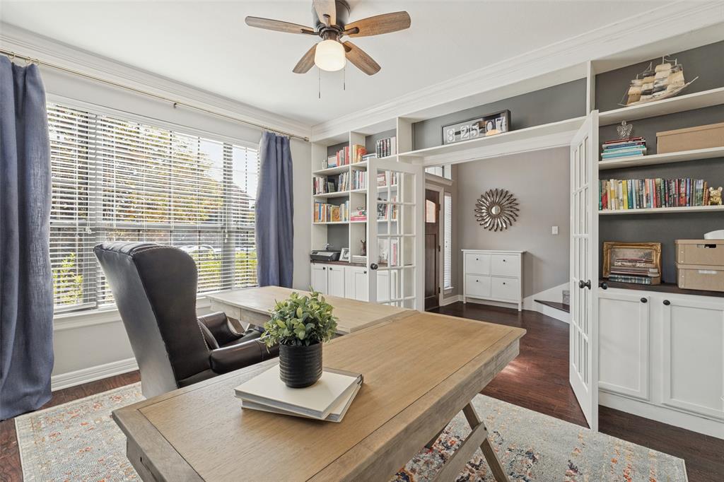 Built-in floor-to-ceiling cabinetry, glass-paned double doors, wood-finish flooring, crown molding, and a ceiling fan