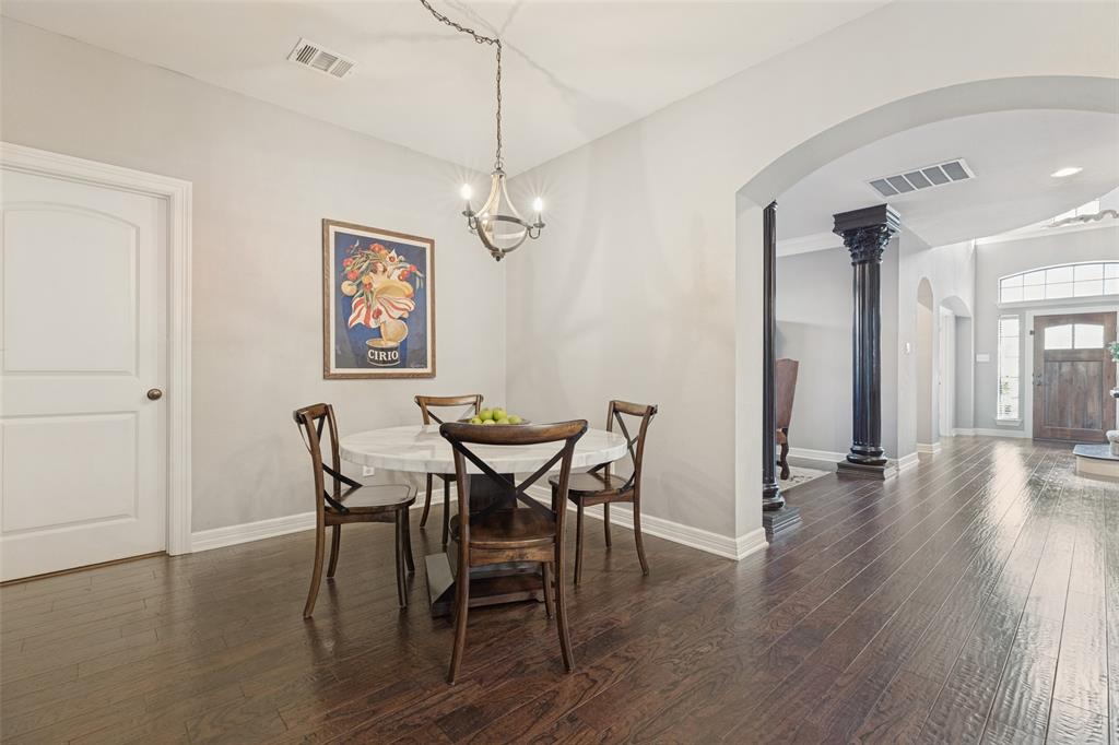 Wood-finish flooring, decorative column, arched entryway, and suspended multi-bulb light fixture