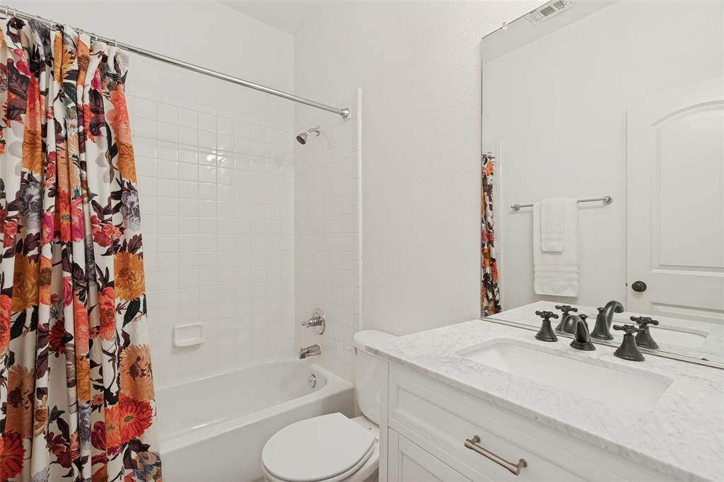 Bathroom for split bedroom featuring a white vanity with a stone-finish countertop, undermount sink, multi-handle faucet, full-height mirror, and a tub with a white tile surround