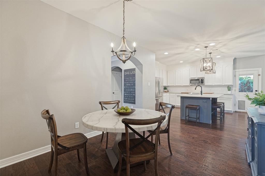 Open-concept area featuring wood-finish flooring, a kitchen island with stone countertop, white shaker-style cabinetry, arched architectural detailing, and dual pendant lighting fixtures