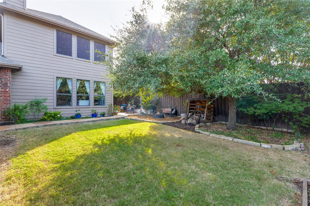 Rear exterior featuring horizontal lap siding, brick masonry detailing, a concrete walkway, and a fenced backyard with mature trees