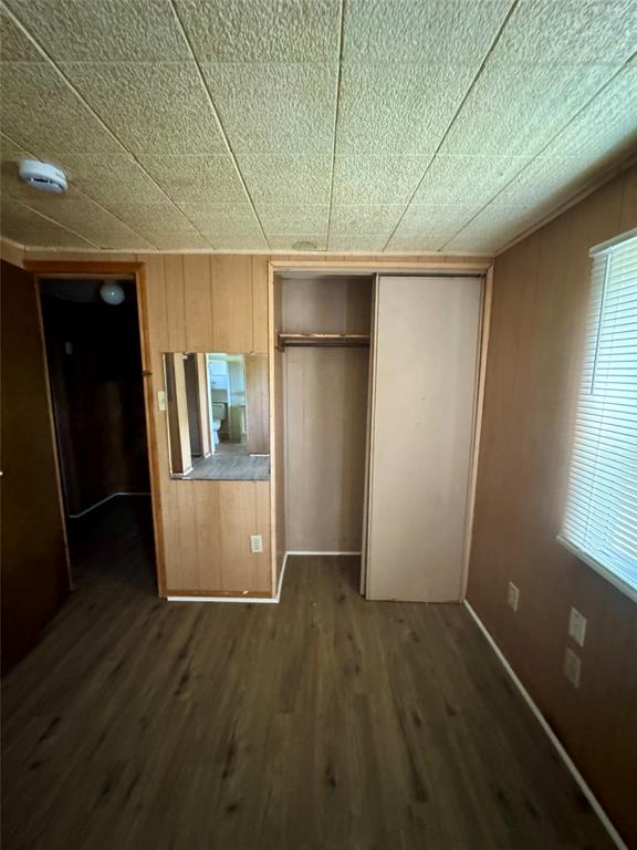 Wood-finish flooring, paneled wall surfacing, ceiling with acoustic-style panels, and built-in closet with sliding panel door