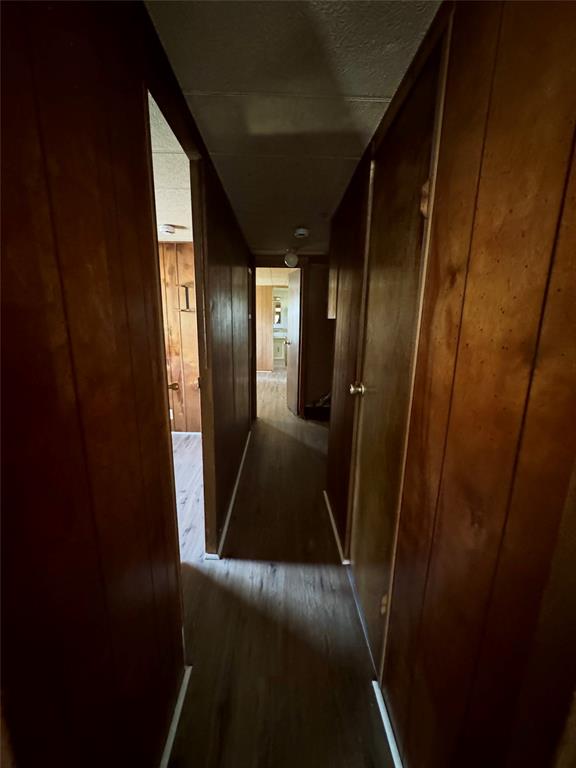 Hallway featuring wood-panel wall finishings, wood-finish flooring, and solid-core doors with metallic hardware