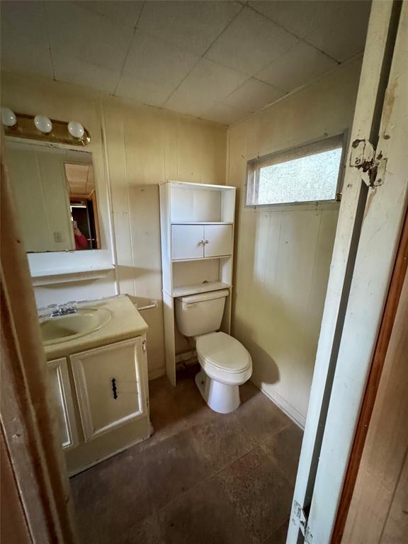 Bathroom featuring a vanity with an integrated sink, wall-mounted light fixture, toilet, built-in vertical storage cabinet, and rectangular hopper window
