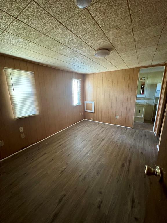 Wood-finish flooring, vertical paneled wall treatments, drop-tile ceiling with flush-mount lighting, and dual windows