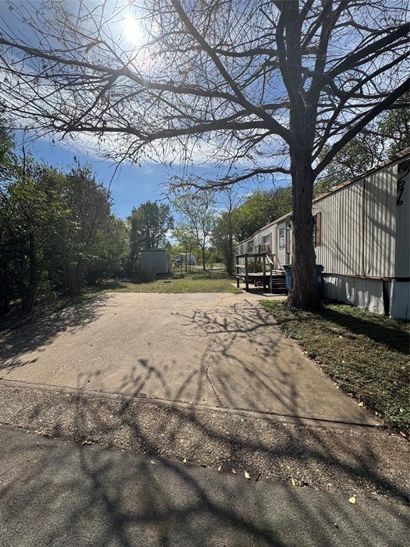 Concrete driveway, level lawn, mature trees, and detached storage structure