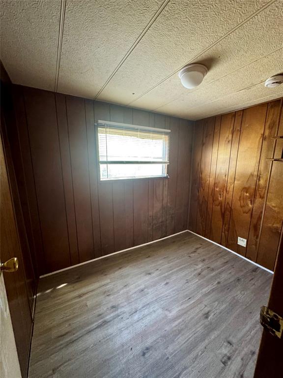 Interior room featuring wood-finish flooring, paneled walls, and a single window with horizontal blinds