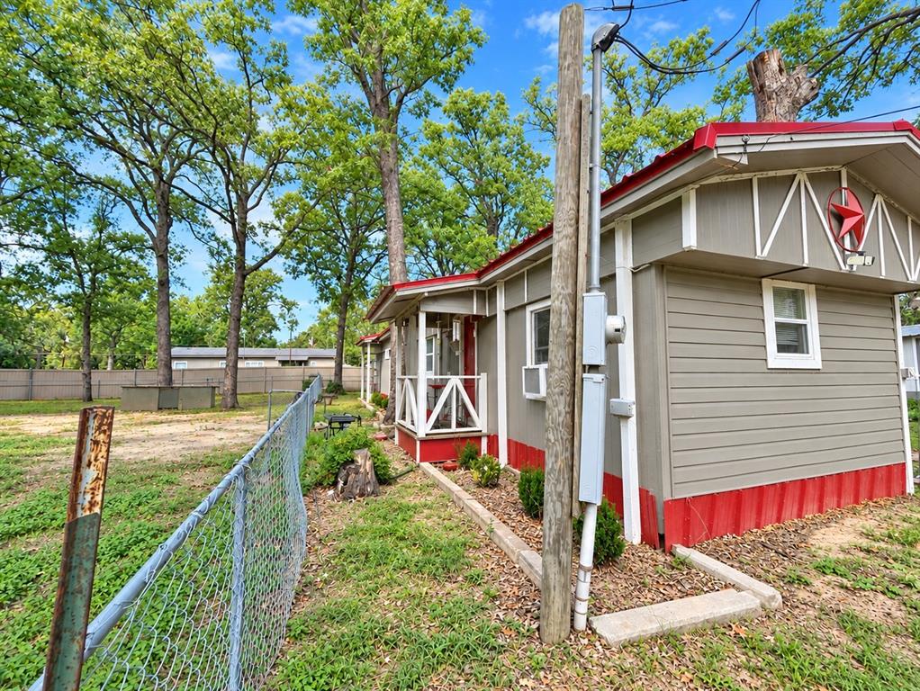 Exterior featuring horizontal siding, a gabled roofline with metal trim, a covered entryway with wood railing, and an expansive lot with mature trees and perimeter chain-link fencing