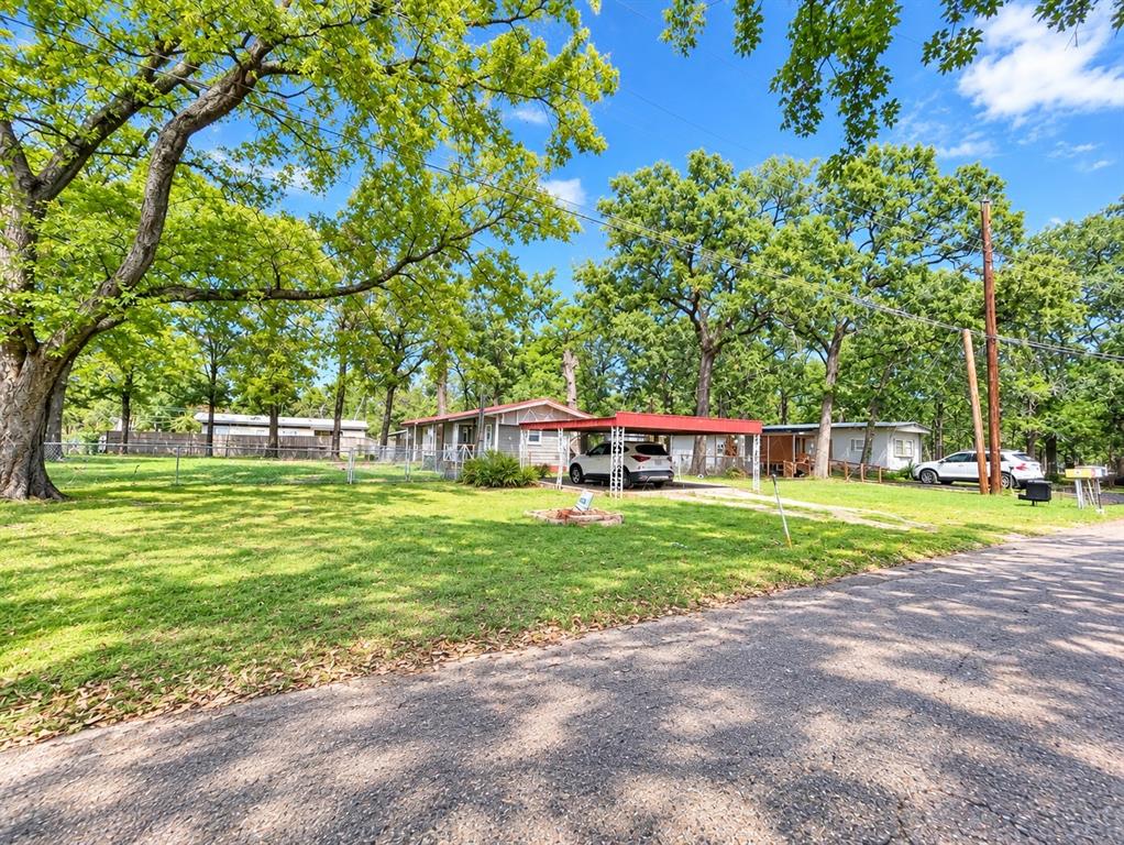 Expansive lot featuring mature trees, chain-link perimeter fencing, and a metal-roofed carport