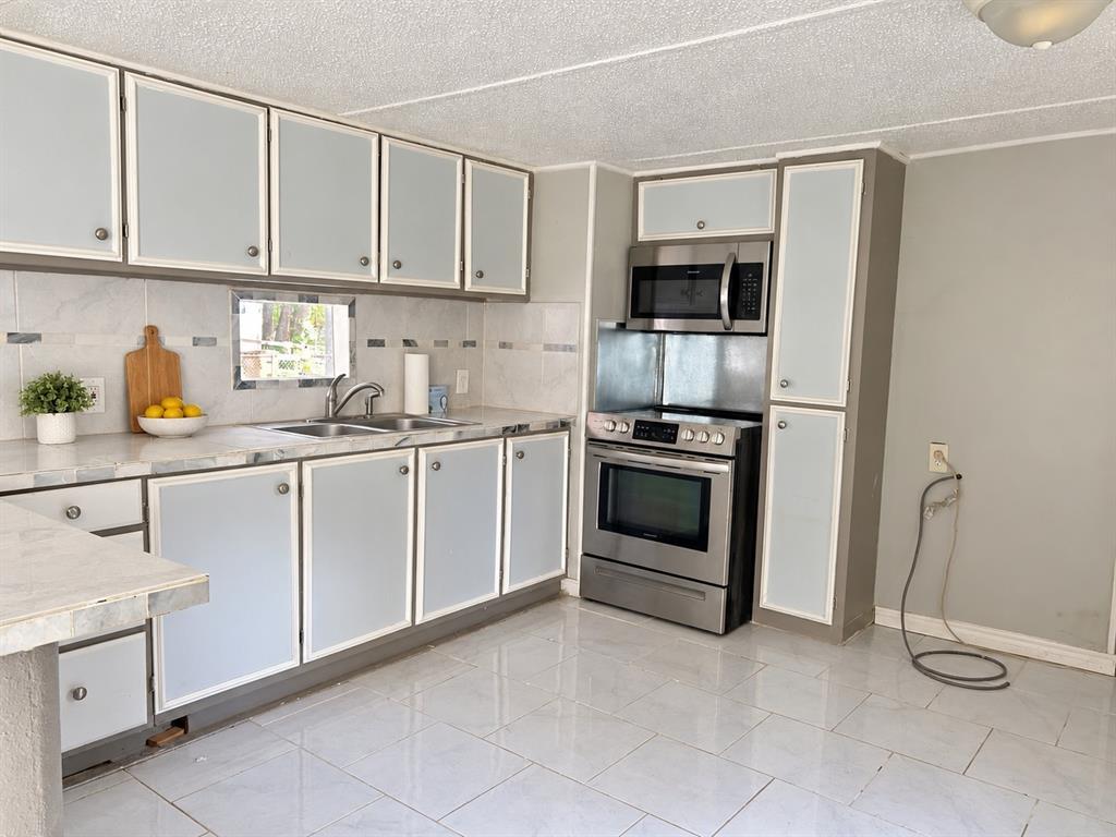 Kitchen featuring cabinetry with frosted glass inserts, stainless steel appliances, a tile backsplash, and light-toned tile flooring