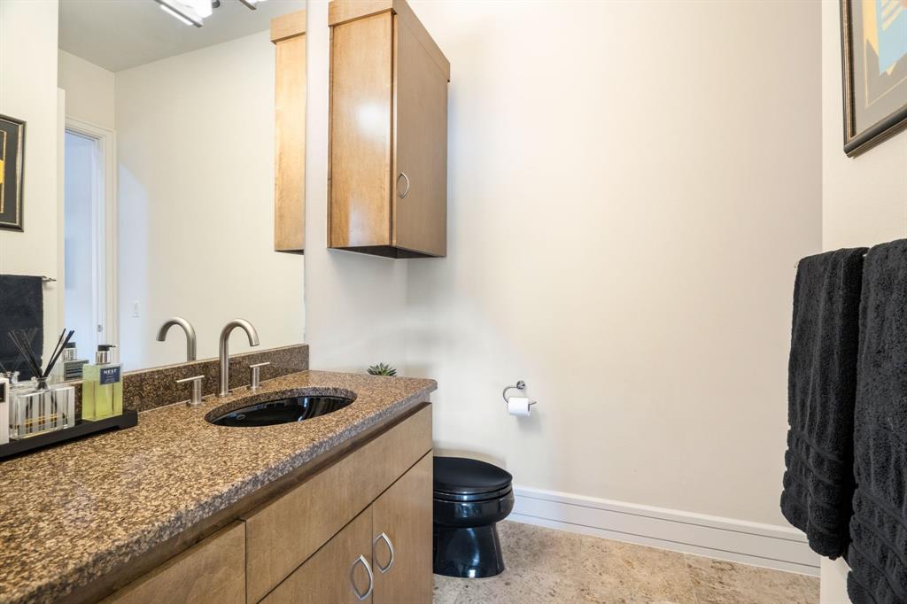 Vanity featuring a stone-finish countertop, undermount oval sink, wooden cabinetry with a wall-mounted storage unit, and a black toilet