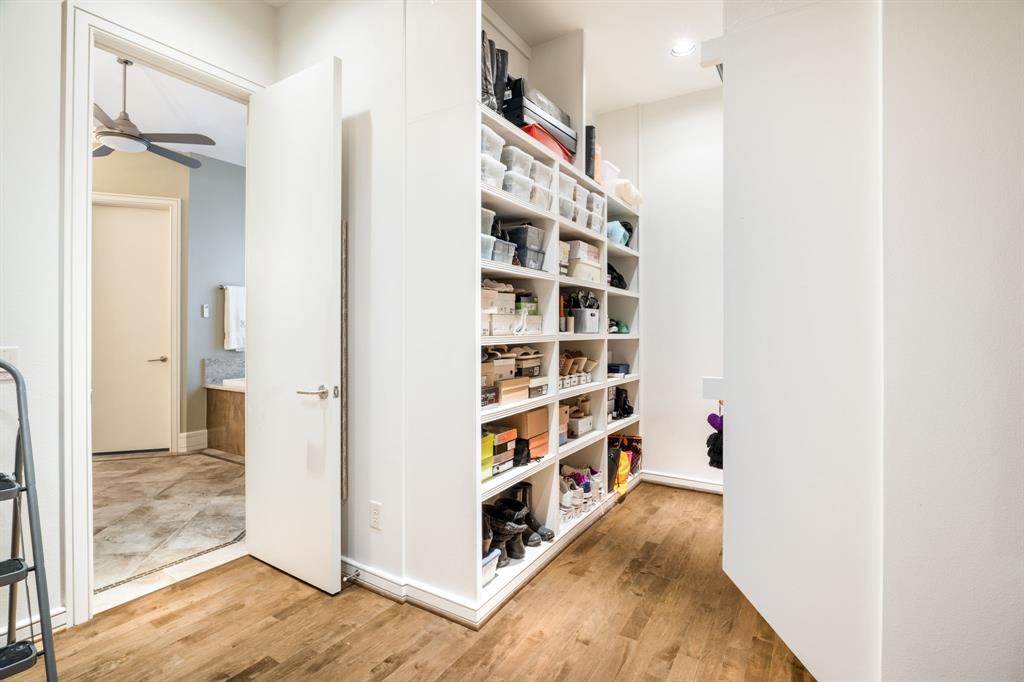 Custom walk-in storage featuring floor-to-ceiling built-in white shelving and wood-finish flooring