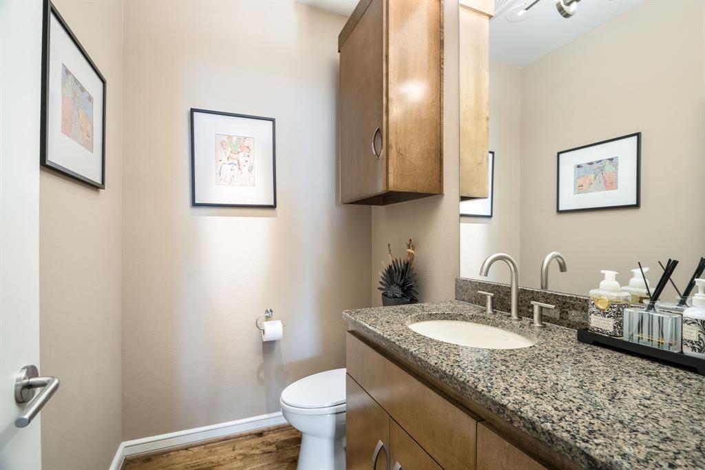 Bathroom featuring a wood-finish vanity with a stone countertop, an integrated sink with a high-arch metal faucet, a wall-mounted wooden cabinet, and wood-finish flooring